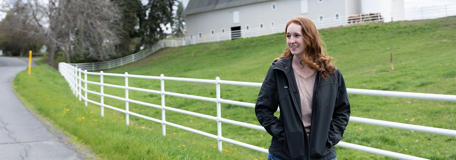 A person standing next to a white fence with a white barn in the background.
